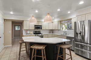 Kitchen featuring appliances with stainless steel finishes, a kitchen island, decorative light fixtures, cream cabinets, and sink