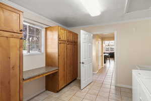 Kitchen featuring a textured ceiling, light tile patterned flooring, washer and dryer, and crown molding