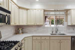 Kitchen featuring sink, tasteful backsplash, cream cabinetry, appliances with stainless steel finishes, and light stone countertops