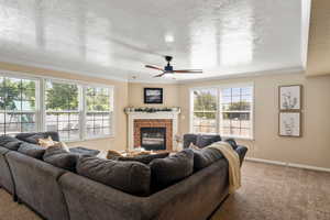 Carpeted living room with ceiling fan, crown molding, a fireplace, and a textured ceiling