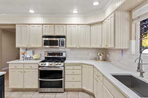 Kitchen featuring sink, appliances with stainless steel finishes, light tile patterned floors, crown molding, and cream cabinets