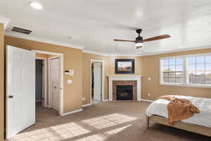 Carpeted bedroom with ceiling fan, a brick fireplace, and crown molding