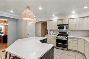 Kitchen featuring hanging light fixtures, stainless steel appliances, an inviting chandelier, a center island, and cream cabinets