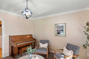 Living area with an inviting chandelier, carpet floors, and crown molding