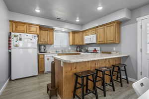 Kitchen featuring sink, kitchen peninsula, a kitchen breakfast bar, light hardwood / wood-style flooring, and white appliances