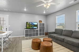 Living room featuring ceiling fan, a textured ceiling, light wood-type flooring, and a wealth of natural light