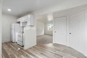 Kitchen featuring white appliances, light wood-type flooring, and white cabinetry