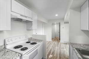 Kitchen featuring light stone counters, light hardwood / wood-style floors, electric range, sink, and white cabinetry