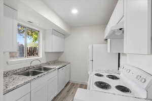 Kitchen featuring light stone counters, white cabinets, white appliances, light hardwood / wood-style flooring, and sink