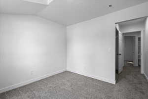 Unfurnished room with dark colored carpet and vaulted ceiling