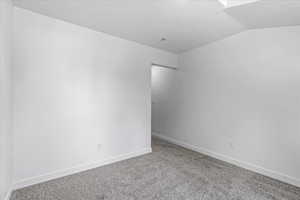 Carpeted spare room featuring vaulted ceiling