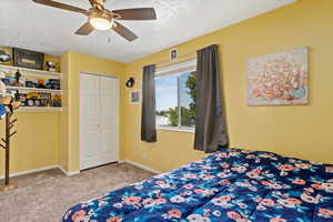 Bedroom with ceiling fan, a textured ceiling, a closet, and carpet