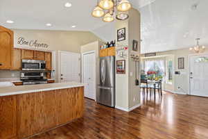 Kitchen with lofted ceiling, dark hardwood / wood-style flooring, stainless steel appliances, and a notable chandelier