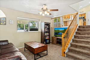 Carpeted living room with ceiling fan and a textured ceiling