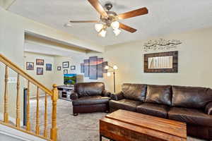 Carpeted living room featuring ceiling fan and a textured ceiling