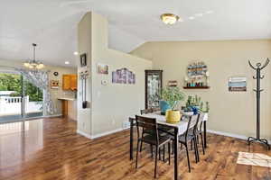 Dining space with lofted ceiling, dark hardwood / wood-style floors, and a notable chandelier