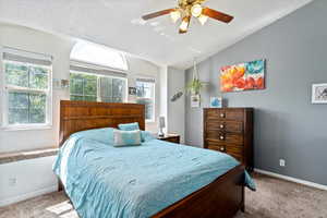 Carpeted bedroom featuring vaulted ceiling, multiple windows, and ceiling fan