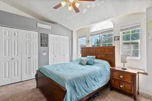 Carpeted bedroom with ceiling fan, lofted ceiling, two closets, and multiple windows