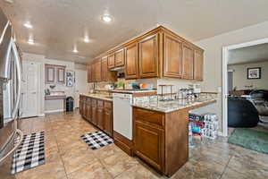 Kitchen featuring light tile patterned flooring, light stone counters, stainless steel refrigerator, dishwasher, and a textured ceiling