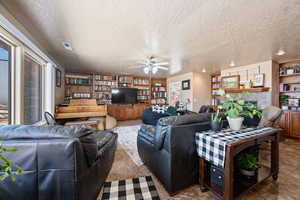 Living room with built in shelves, ceiling fan, and a textured ceiling