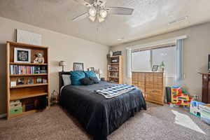 Carpeted bedroom featuring ceiling fan and a textured ceiling