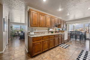 Kitchen with a textured ceiling, light tile patterned flooring, ceiling fan, and light stone counters