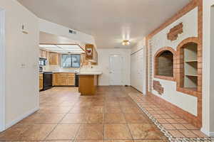 Kitchen with a textured ceiling, black appliances, and light tile patterned flooring