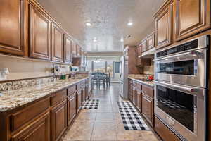 Kitchen with a textured ceiling, appliances with stainless steel finishes, light tile patterned floors, light stone countertops, and ceiling fan