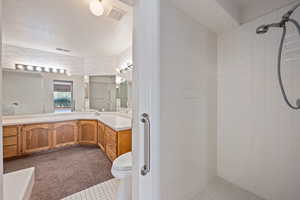 Bathroom featuring vanity, toilet, a textured ceiling, and tiled shower