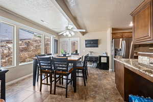 Dining space featuring a textured ceiling, beamed ceiling, ceiling fan, and dark tile patterned flooring