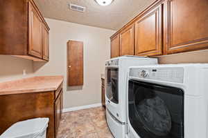 Laundry area featuring a textured ceiling, light tile patterned flooring, washing machine and clothes dryer, and cabinets