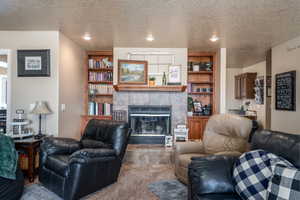 Carpeted living room featuring built in shelves, a tiled fireplace, and a textured ceiling