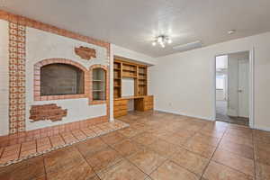 Unfurnished living room with built in desk, a textured ceiling, tile patterned floors, and built in features