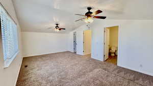 Unfurnished bedroom featuring connected bathroom, vaulted ceiling, light carpet, and ceiling fan