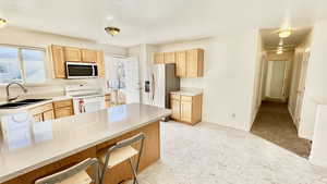 Kitchen with a breakfast bar area, sink, kitchen peninsula, stainless steel appliances, and light brown cabinetry