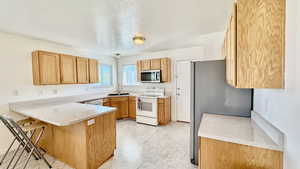 Kitchen featuring a breakfast bar, kitchen peninsula, stainless steel appliances, a textured ceiling, and sink