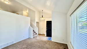 Spare room with light colored carpet, a textured ceiling, a chandelier, and high vaulted ceiling