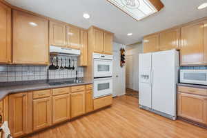 Kitchen featuring decorative backsplash, white appliances, and light hardwood / wood-style flooring