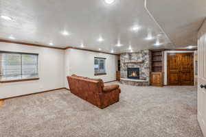 Living room with light carpet, a stone fireplace, a textured ceiling, and ornamental molding.  Theater room behind double doors.