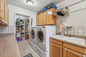 Laundry area with light tile patterned floors, sink, washer and dryer, and cabinets