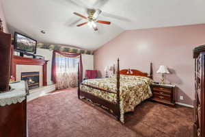 Bedroom with a tile fireplace, vaulted ceiling, ceiling fan, and dark carpet