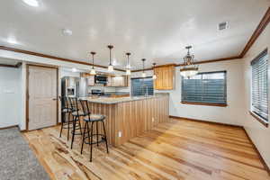 Kitchen with light hardwood / wood-style floors, light stone counters, pendant lighting, stainless steel appliances, and ornamental molding