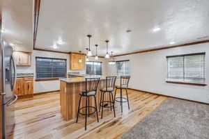 Kitchen featuring hanging light fixtures, light stone counters, light wood-type flooring, stainless steel refrigerator with ice dispenser, and sink