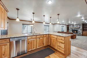 Kitchen with a fireplace, kitchen peninsula, light hardwood / wood-style flooring, stainless steel dishwasher, and sink