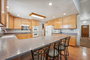 Kitchen with sink, white appliances, backsplash, a kitchen breakfast bar, and light hardwood / wood-style floors