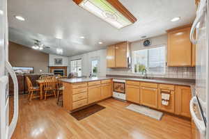 Kitchen with vaulted ceiling, tasteful backsplash, kitchen peninsula, ceiling fan, and light hardwood / wood-style flooring