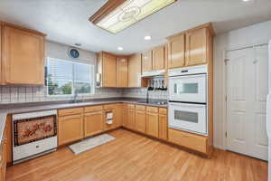 Kitchen featuring light wood-type flooring, dishwasher, tasteful backsplash, sink, and double oven