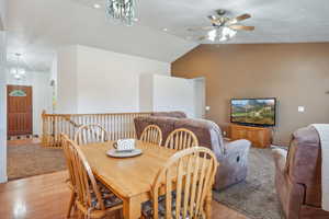 Dining room with light wood-type flooring, ceiling fan with notable chandelier, and lofted ceiling