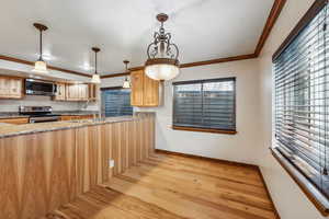 Kitchen with light wood-type flooring, appliances with stainless steel finishes, decorative light fixtures, ornamental molding, and light brown cabinetry