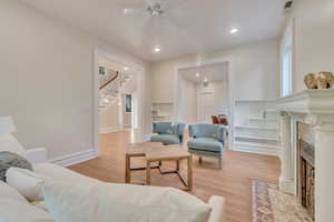 Living room with a fireplace, ceiling fan, and light hardwood / wood-style flooring